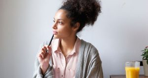 A woman is thinking with a pen by her mouth