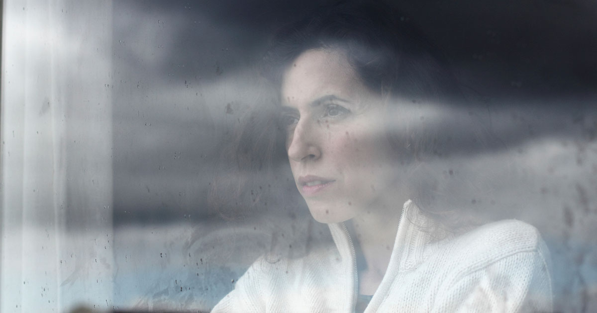 A woman is looking through a foggy window with a sad expression